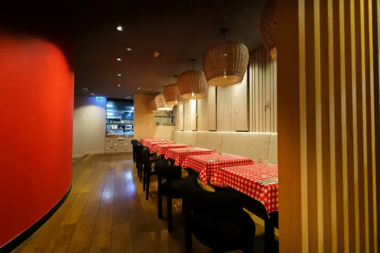 A long dining room with a red wall and checked tablecloths at Mama's & Papa's